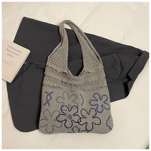 Detail of grey knitted tote bag with blue floral patterns and open mesh texture
