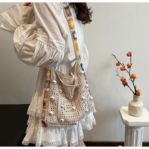 Detail der Boho-Häkeltasche mit Perlenverzierung und Blumen-Strickgurt vor weißem Kleid