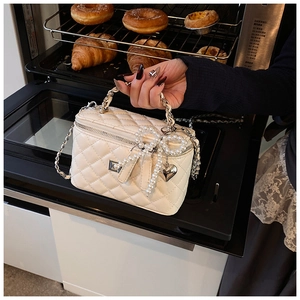 Detailed view of white quilted box bag with pearl bow, silver heart charm and chain