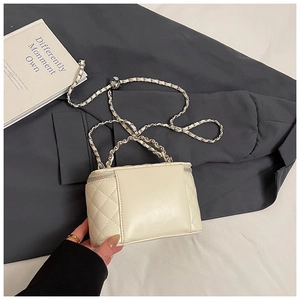 Detail of a quilted cream vanity bag with a leather woven chain on a grey blazer