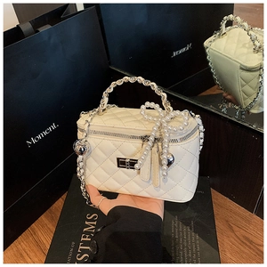 Detail of cream quilted box bag featuring pearl bow chain and silver metallic clasp