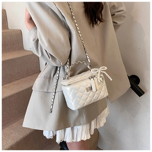 Detail of white quilted box bag featuring pearl bow charm and silver chain strap