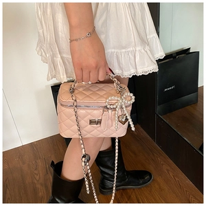 Detail of pink quilted crossbody bag with pearl bow charm and metal heart pendant