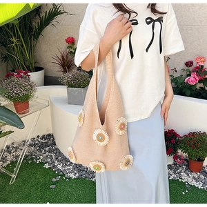 Detailed macro view of 3D knit daisies on a cream shoulder tote bag in an outdoor setting