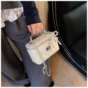Detail of white quilted box bag featuring a pearl bow handle and silver chain strap