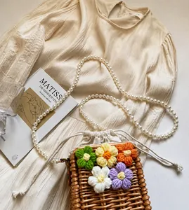 Détail du sac seau en paille tissée avec fleurs en tricot et élégante bandoulière en perles