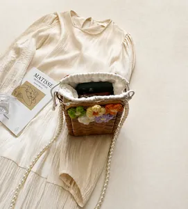 Détail du sac seau en paille avec fleurs au crochet colorées et bandoulière en perles