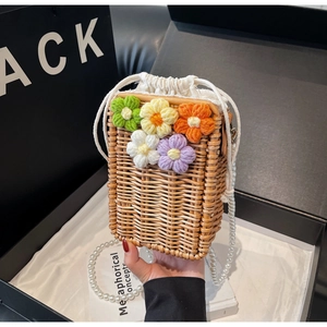 Détail d'un sac seau en paille avec fleurs au crochet et bandoulière en perles