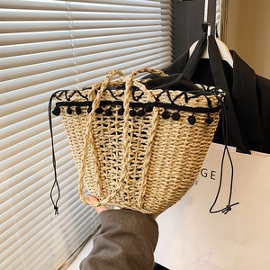 Handmade woven straw bucket bag with black pompom trim and drawstring closure for vacation