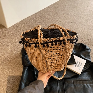 Handwoven straw tote bag with black pom-pom trim and drawstring liner for beach vacations