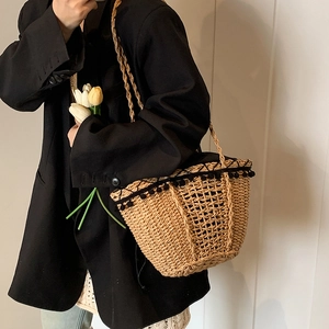 Handmade straw basket bag with black pom-pom trim and long straps for beach vacation