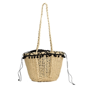 Handmade woven straw bag with black pom-poms and drawstring closure for summer beach vacation