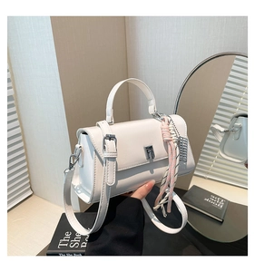 Close-up of white leather handbag with silver lock and woven pendant on wooden desk
