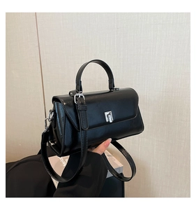 Detail of a minimalist black top-handle bag featuring a silver metal square lock and strap