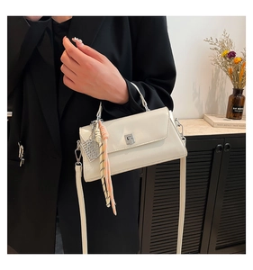 Detail of minimalist cream leather handbag with silver twist lock and woven charm
