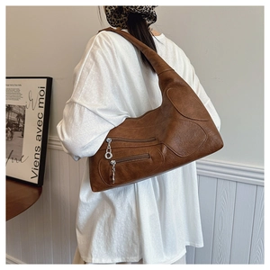 Detail showing vintage brown PU leather texture and metal chain charms on shoulder bag