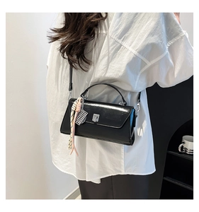 Detail of a black glossy crossbody bag with silver rotating lock and colorful knotted charm