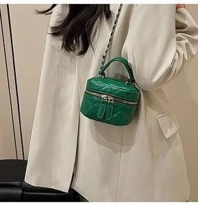 Detail of green quilted mini bag with double zippers and gold chain strap on beige blazer
