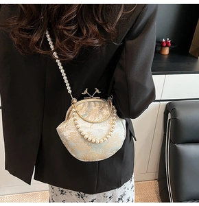 Detail of vintage evening bag featuring gold embroidery and pearl strap worn with black suit