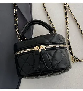 Detail of mini quilted crossbody bag with gold zippers and chain strap on grey fabric