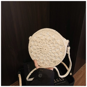 Detail of hand-woven round straw bag with hollow sun flower pattern and beige strap