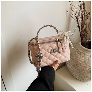 Pink quilted vanity box bag with chain handle and pearl bow detail in a minimalist setting
