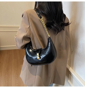 Detail view of a black crescent shoulder bag with glossy leather and gold chain decoration