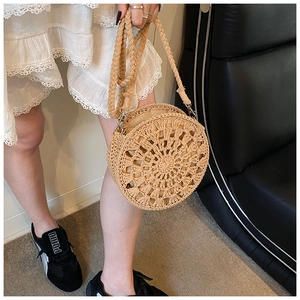 Detailed close-up of a round straw woven crossbody bag featuring intricate hollow patterns