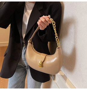 Detail of beige crescent bag with glossy finish and gold chain shoulder strap