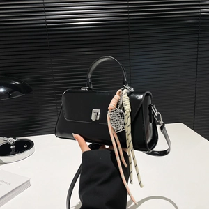 Minimalist black patent leather handbag with silver clasp and woven charm on desk