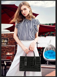 Fashionable black crocodile embossed tote bag held by model in an outdoor cafe setting