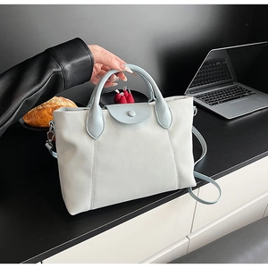 Detail of grey lychee leather tote bag with blue contrast handle on a minimalist desk
