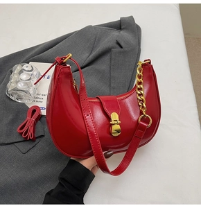 Detail of red crescent hobo bag with glossy finish and decorative gold chain strap