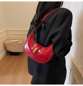 Detail of red patent leather crescent bag with gold buckle worn on the shoulder