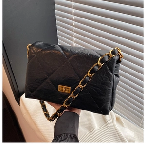 Detail of black quilted shoulder bag with glossy texture and gold-tone chain strap