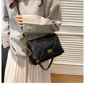 Detail of black quilted puffer crossbody bag featuring a gold turn-lock and chain strap