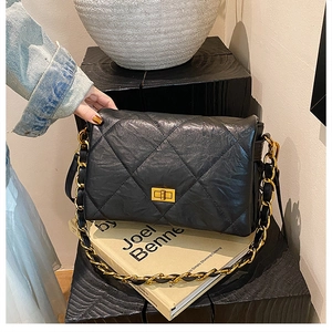 Close-up of black quilted leather shoulder bag with golden twist-lock and chain strap
