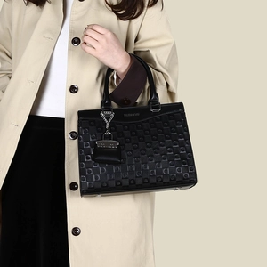 Detail of black tote bag featuring embossed geometric patterns and a silver chain charm