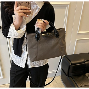 Detail of dark brown canvas tote bag with black glossy leather flap and adjustable strap