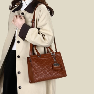 Detail of dark brown tote bag featuring geometric embossed texture and leather charm