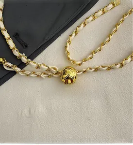 Close-up of golden ball strap adjuster on quilted chain handbag with white leather