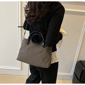 Detail view of taupe tote bag with black handles and detachable shoulder strap on model