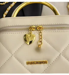 Detail of cream quilted handbag with gold circular handle and heart-shaped zipper pull
