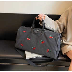 Close-up of black canvas tote bag featuring red cherry embroidery and leather handles