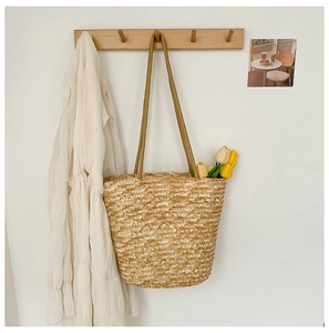 Detail of hand-woven straw bucket bag texture and straps against a minimalist wall