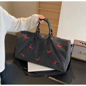 Detail of black canvas tote bag with red cherry embroidery and leather handles on table