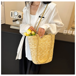 Detailed close-up of handmade woven straw bucket bag with intricate texture and shoulder strap