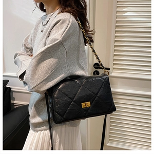 Detail of black quilted shoulder bag with gold clasp and chain strap on a model