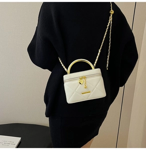 Detail of white quilted crossbody bag featuring golden heart charm and metal handle