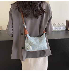 Detail of blue denim pillow bag with ribbon bow and brown adjustable shoulder strap
